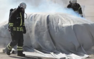 Feuerwehr setzt Brandbegrenzungsdecke E-Auto ein, um Rauchentwicklung zu reduzieren.