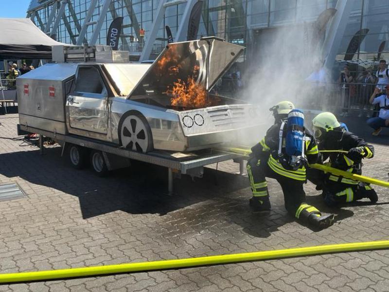 Zwei Feuerwehrleute schieben den FIREdown SprayJet unter ein Fahrzeug, das auf einer Messe ein brennendes Auto darstellen soll